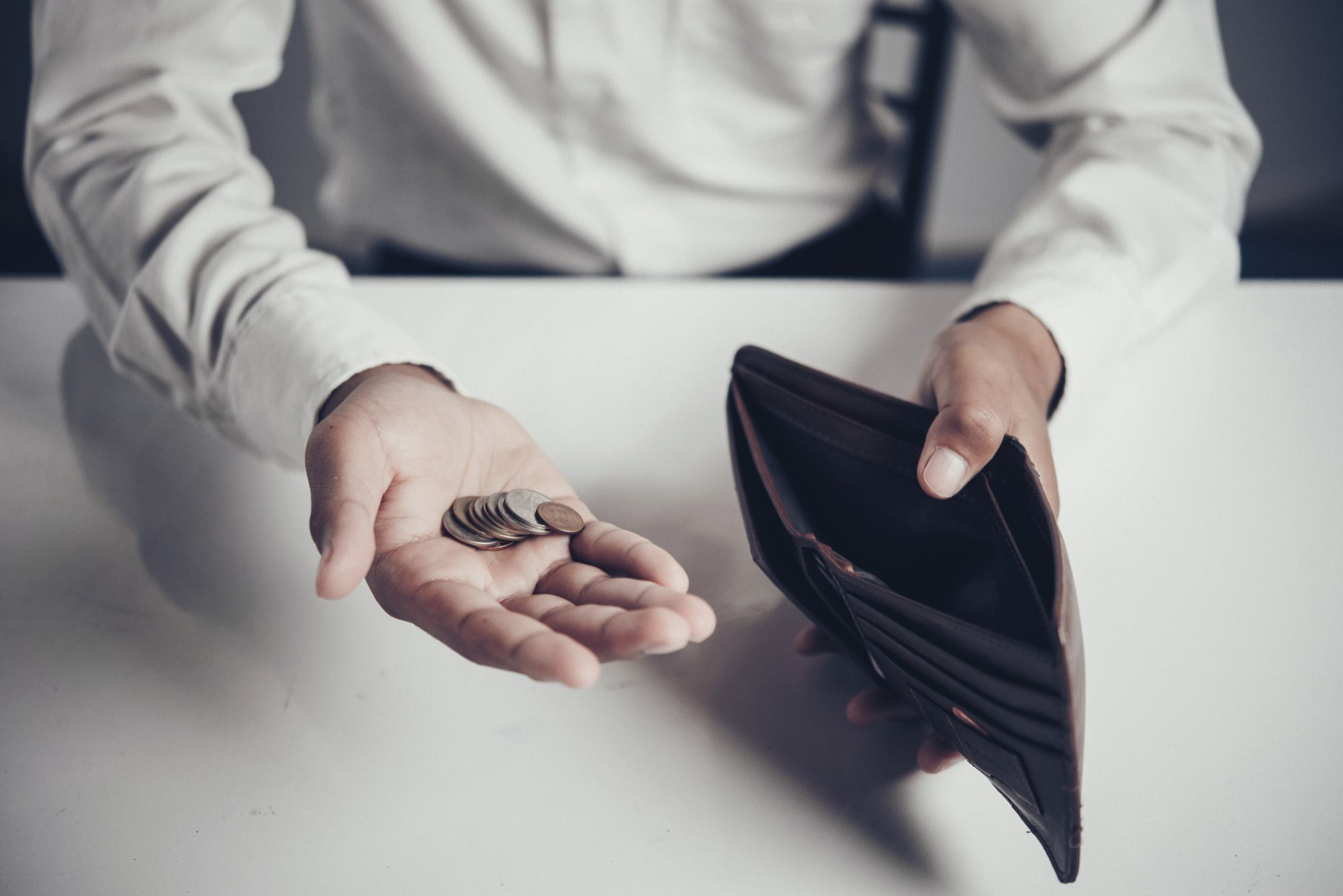 Un hombre sujeta una cartera vacía con unas monedas en la mano.