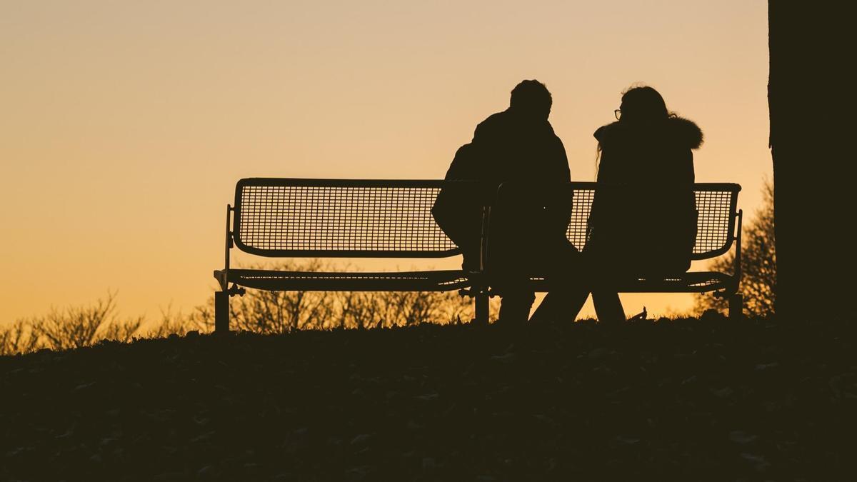 Una pareja sentada en un banco contempla el atardecer.