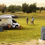 Autocaravana estacionada en un campo junto a una familia y una estación de energía portáti