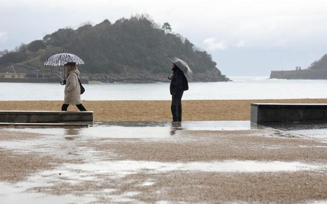 Dos personas pasean por la playa de la Concha durante un temporal de lluvia y frío.