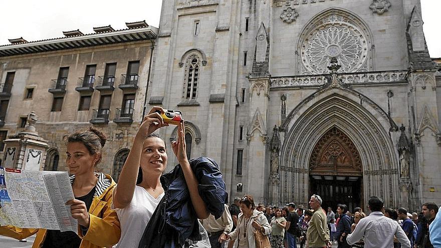 Dos jóvenes se hacen un selfi y consultan un mapa turístico junto a la catedral de Santiago, durante una visita a Euskadi. | FOTO: PABLO VIÑAS