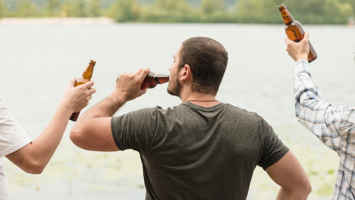 Un hombre bebe una cerveza del botellín con amigos.