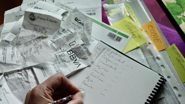 Una persona haciendo la contabilidad el hogar rodeada de etiquetas de compra y facturas
