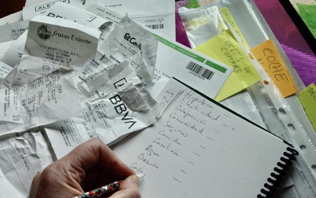 Una persona haciendo la contabilidad el hogar rodeada de etiquetas de compra y facturas