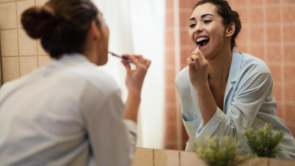 Una mujer se cepilla los dientes frente al espejo del baño.