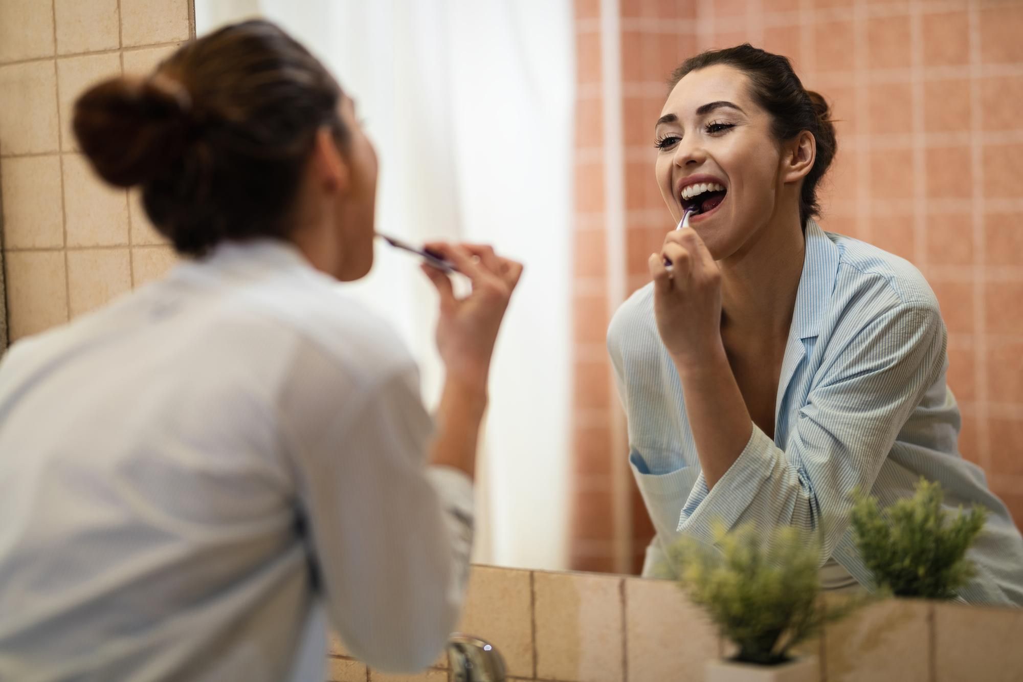Una mujer se cepilla los dientes frente al espejo del baño.