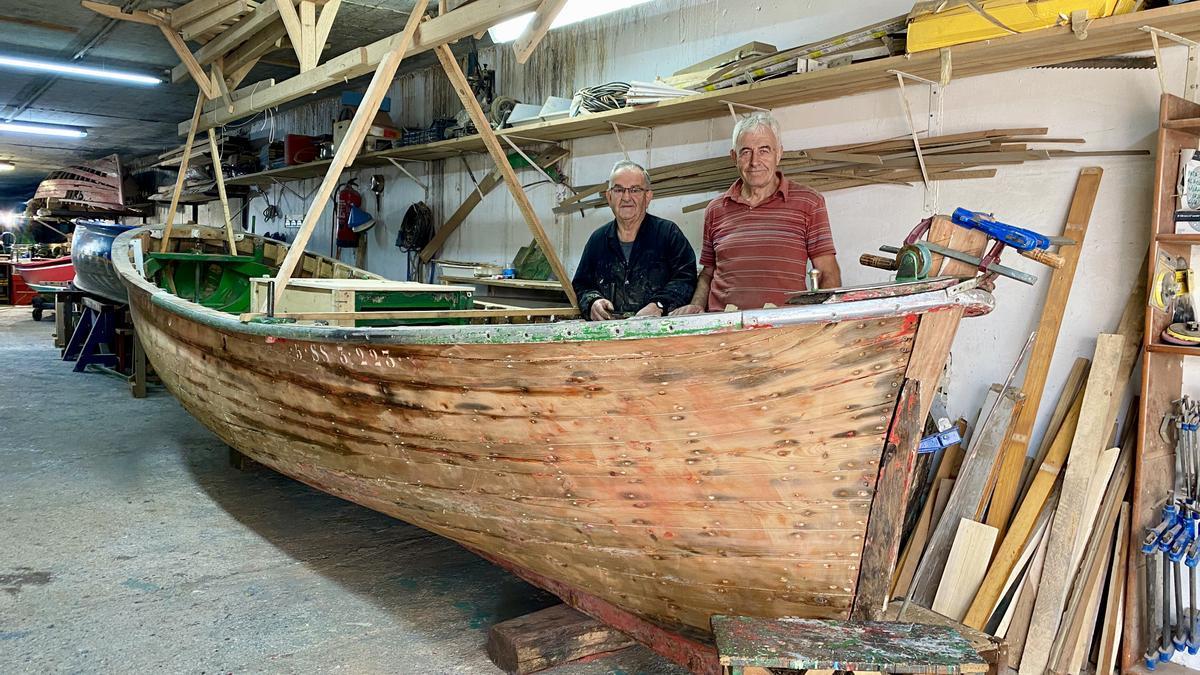 Joxe Osa y Pello Iribar, junto al casco en restauración de la motora 'Jai Txiki' en el taller de Beduola, en Zumaia.