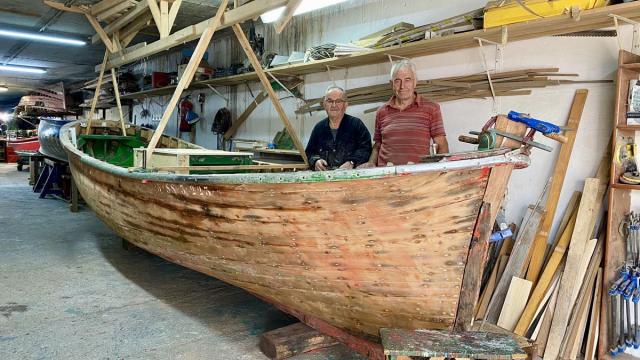 Joxe Osa y Pello Iribar, junto al casco en restauración de la motora 'Jai Txiki' en el taller de Beduola, en Zumaia.