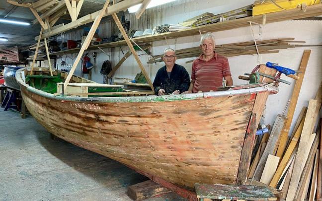 Joxe Osa y Pello Iribar, junto al casco en restauración de la motora 'Jai Txiki' en el taller de Beduola, en Zumaia.