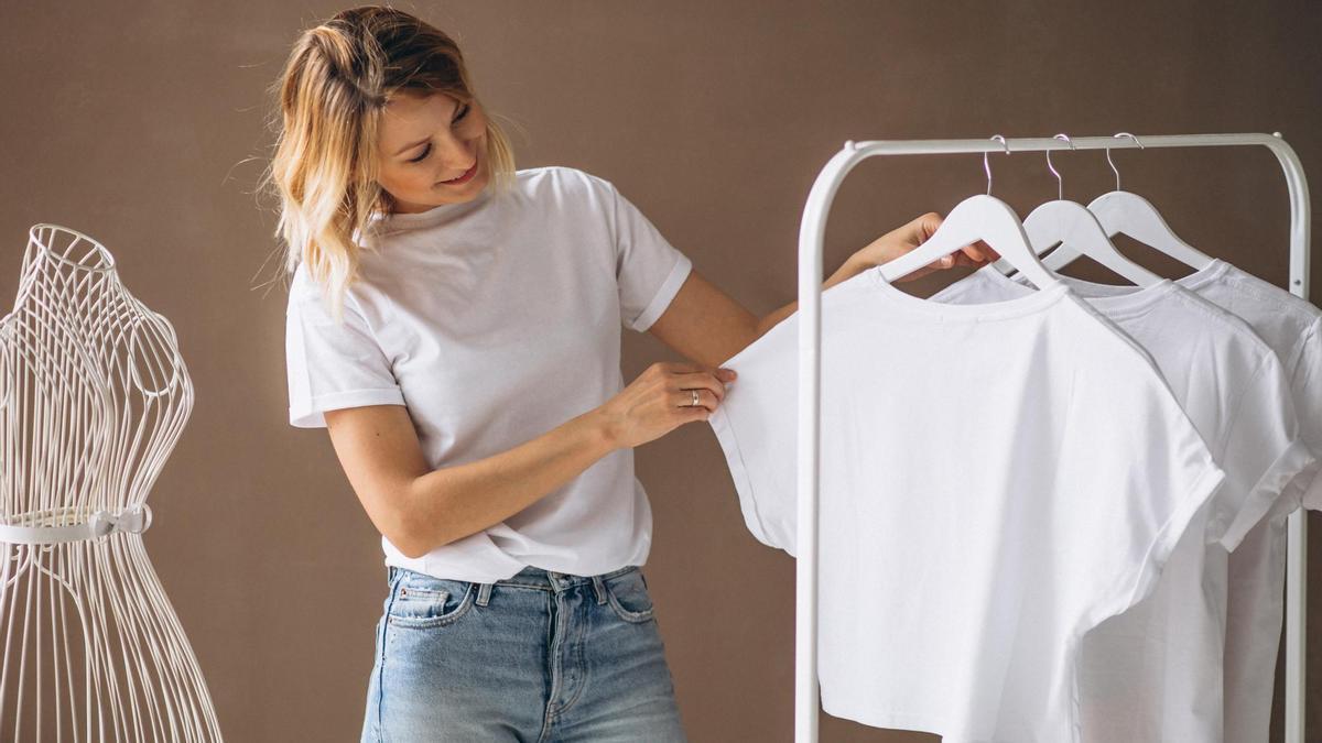 Una mujer mira una camiseta blanca colgada en un perchero.