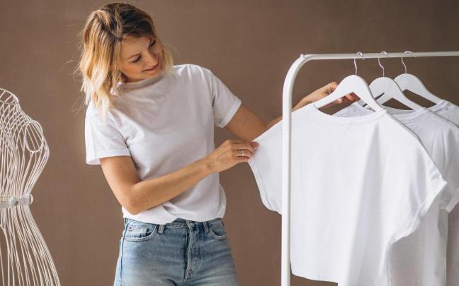 Una mujer mira una camiseta blanca colgada en un perchero.