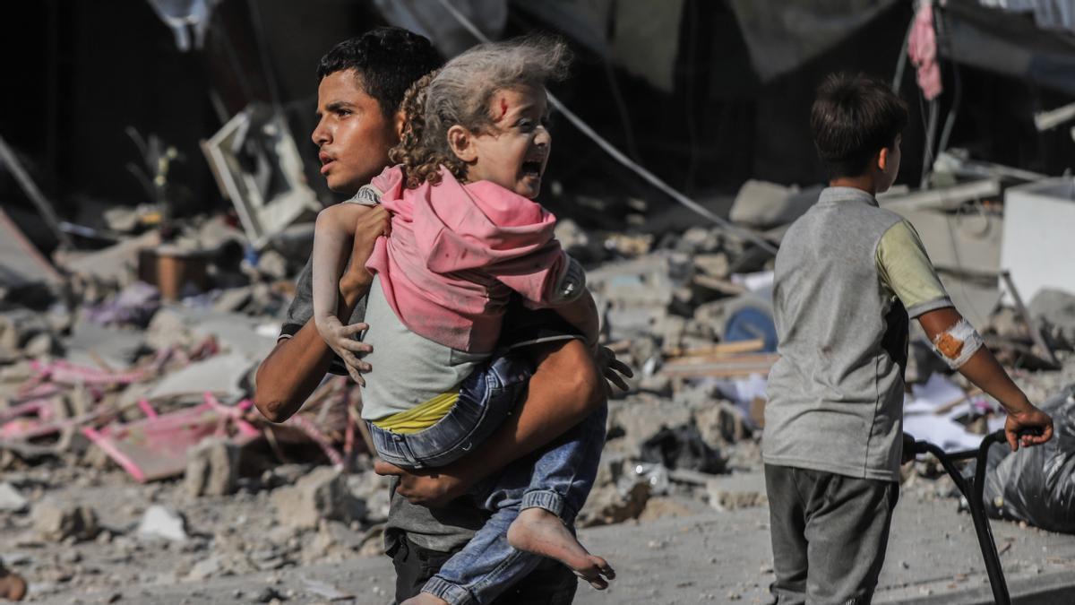Un joven carga en brazos con una niña herida en un bombardeo israelí en Gaza.