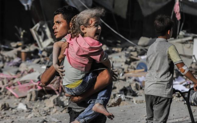 Un joven carga en brazos con una niña herida en un bombardeo israelí en Gaza.