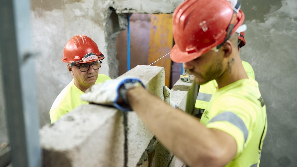 Dos albañiles trabajan levantando un tabique.