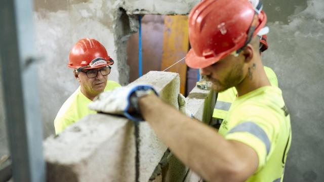 Dos albañiles trabajan levantando un tabique.