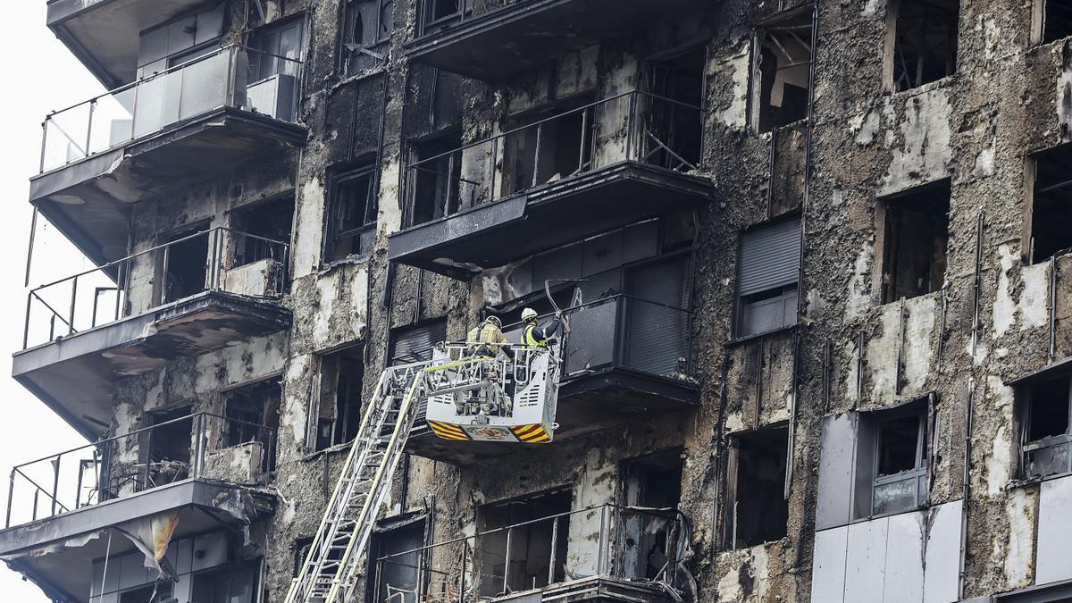 Bomberos en una grúa sanean la fachada quemada.