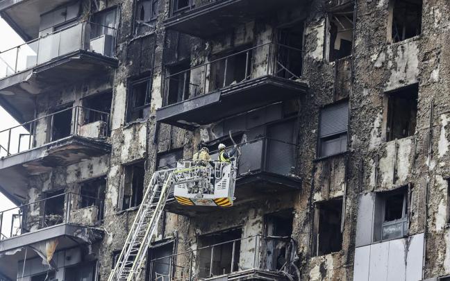 Bomberos en una grúa sanean la fachada quemada.