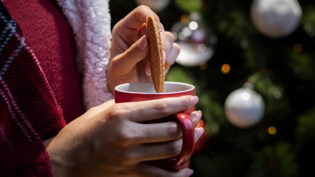 Mujer moja una gallea en una taza con el árbol de Navidad de fondo