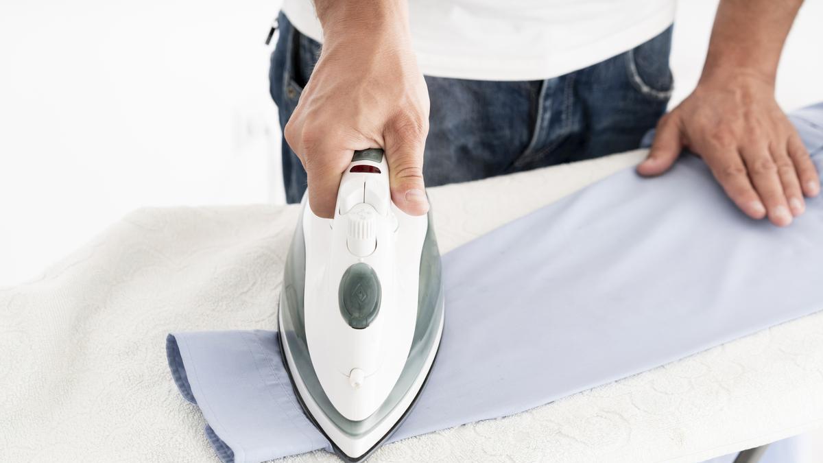 Hombre plancha una camisa de color azul.