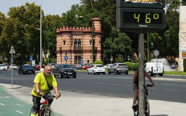 Un hombre circula en bicicleta por Sevilla junto a un termómetro que marca 46 grados.