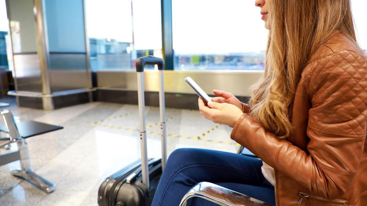 Una mujer utiliza su teléfono móvil mientras espera en un aeropuerto.