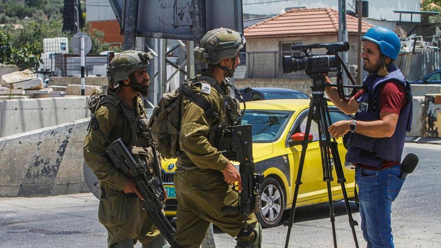 Soldados israelíes impiden trabajar a un periodista mientras vigilan la calle en la localidad de Deir Sharaf, cerca de Nablus.
