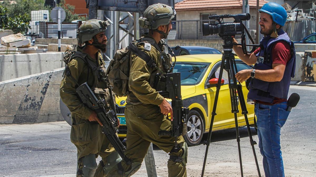 Soldados israelíes impiden trabajar a un periodista mientras vigilan la calle en la localidad de Deir Sharaf, cerca de Nablus.