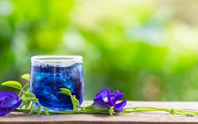 Un vaso de té azul junto a flores de guisante de mariposa. Un vaso de té azul junto a flores de guisante de mariposa.