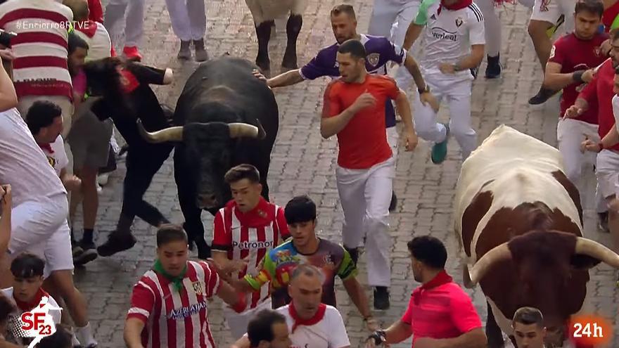 Una chica con camiseta oscura se lleva un importante golpe en la bajada del Callejón y se libra por poco del pitón derecho de un miura.