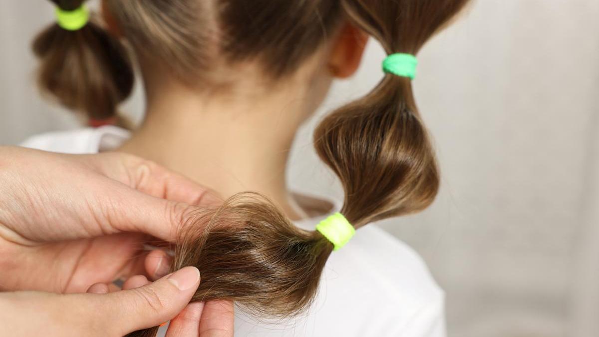 Madre hace un peinado a su hija con gomas del pelo de color verde.