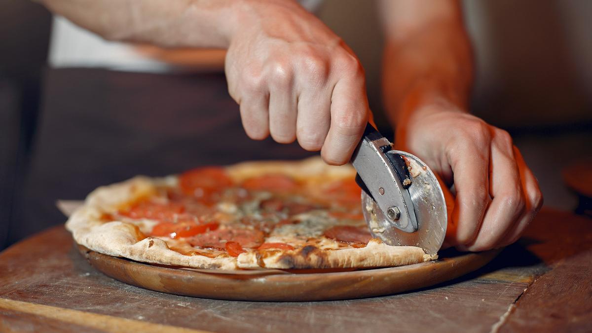 Una persona corta una pizza con un cortador de rueda.