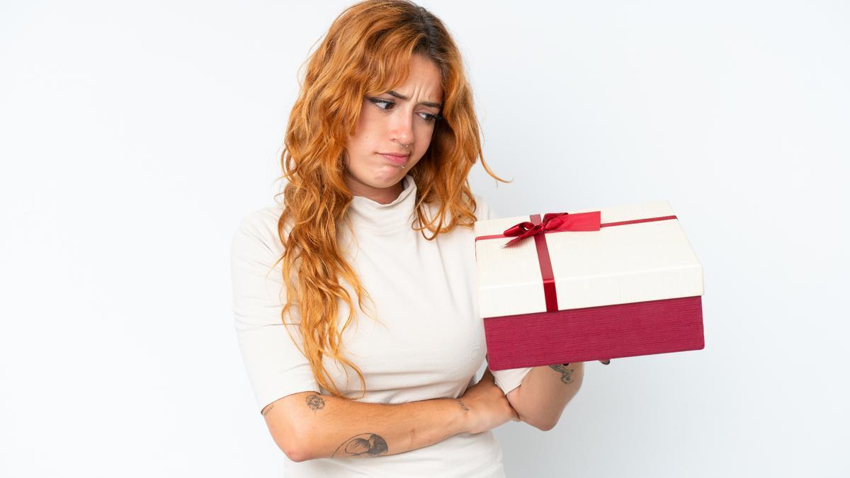 Una mujer sujeta un regalo con cara de decepción.