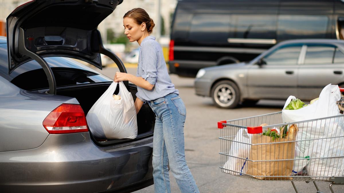 Una mujer traslada sus compras del carro al maletero de su coche.