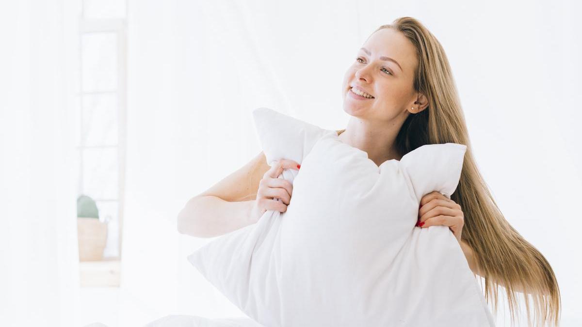 Chica sonriente sostiene una almohada con las manos.