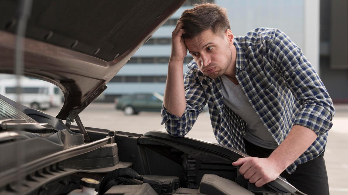 Un joven mira con resignación el motor de su coche.