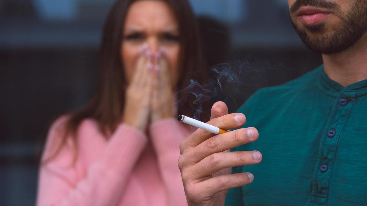 Una mujer se tapa la nariz mientras un hombre fuma un cigarrillo.
