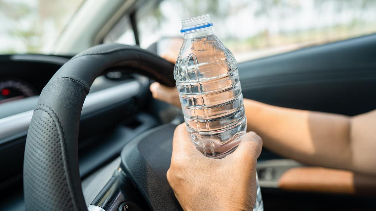 Una persona sostiene una botella de agua en el interior de sus coche.