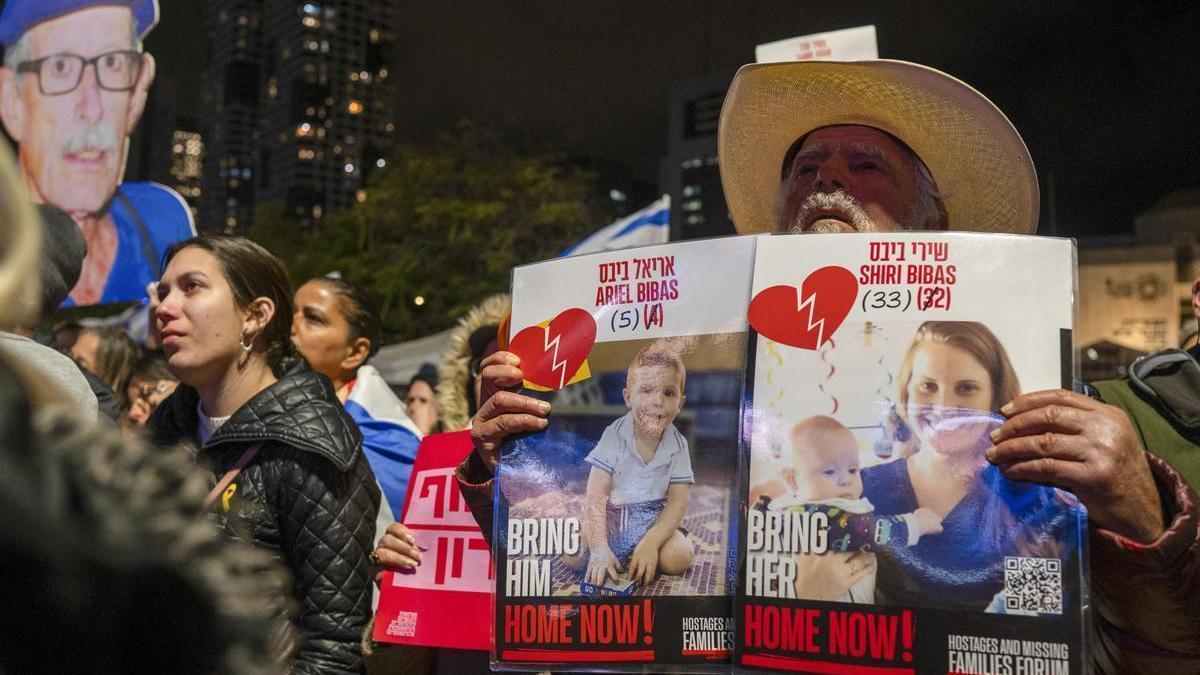 Un hombre sujeta dos carteles con las imágenes de Shiri Bibas y sus hijos en una concentración en Tel Aviv.