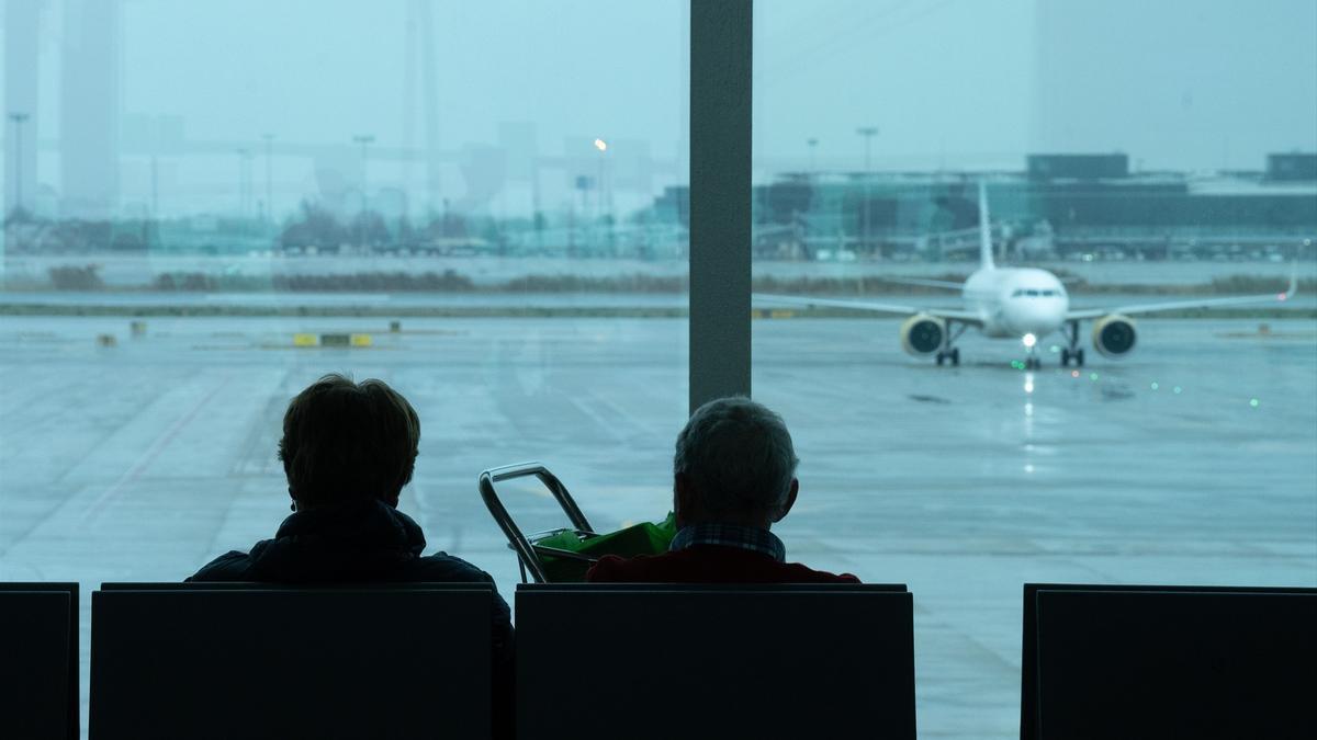 Dos personas esperan sentadas frente a un avión.