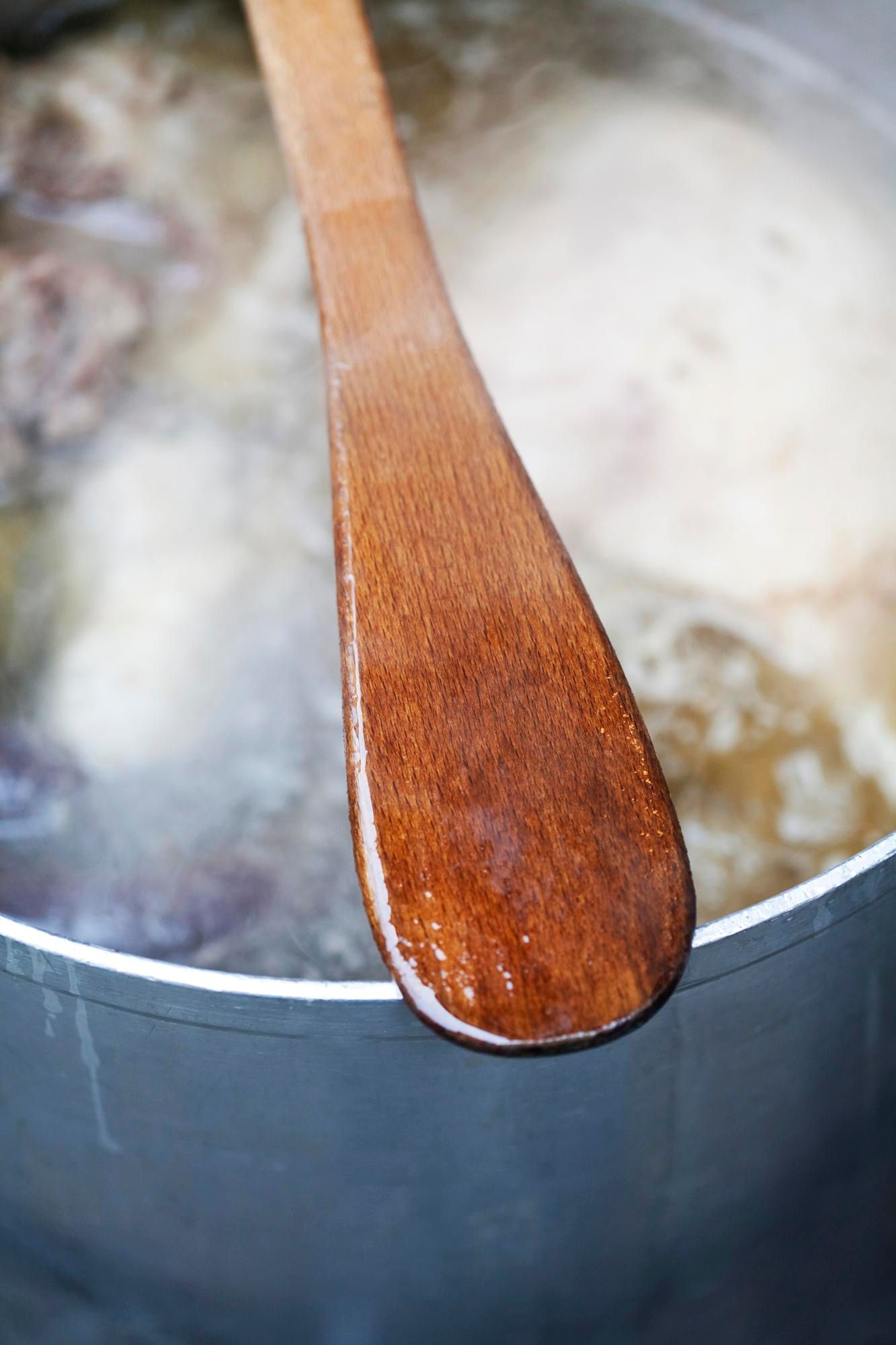 Una cuchara de madera sobre una olla con agua hirviendo.