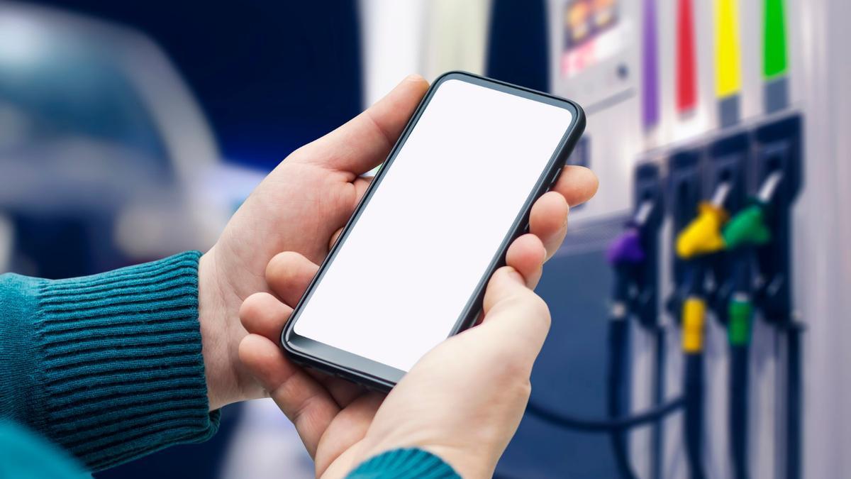 Una persona mira su teléfono móvil frente a los surtidores de una gasolinera.