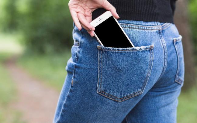 Una mujer guarda el móvil en el bolsillo trasero del pantalón. Una mujer guarda el móvil en el bolsillo trasero del pantalón.