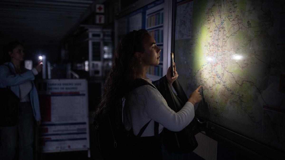 Una mujer ilumina con la linterna del móvil un plano de la red de Metro de Madrid durante el apagón.