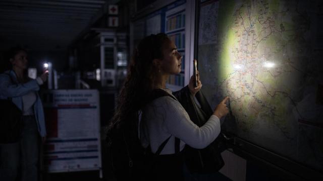 Una mujer ilumina con la linterna del móvil un plano de la red de Metro de Madrid durante el apagón.