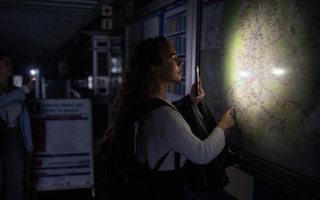 Una mujer ilumina con la linterna del móvil un plano de la red de Metro de Madrid durante el apagón.