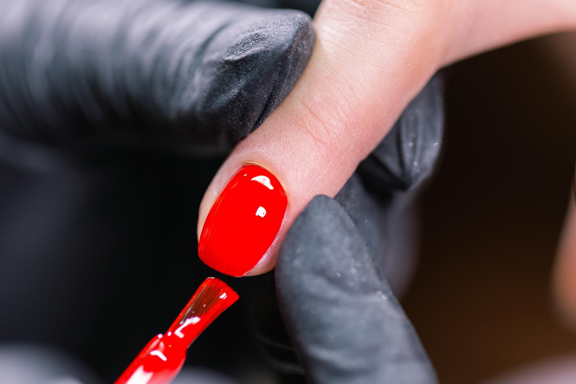Una profesional hace a una clienta una manicura de color rojo.