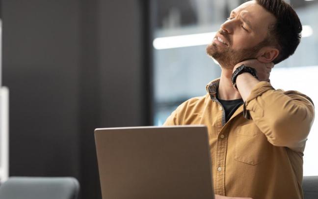 Un hombre presenta dolor cervical mientras trabaja con un ordenador.