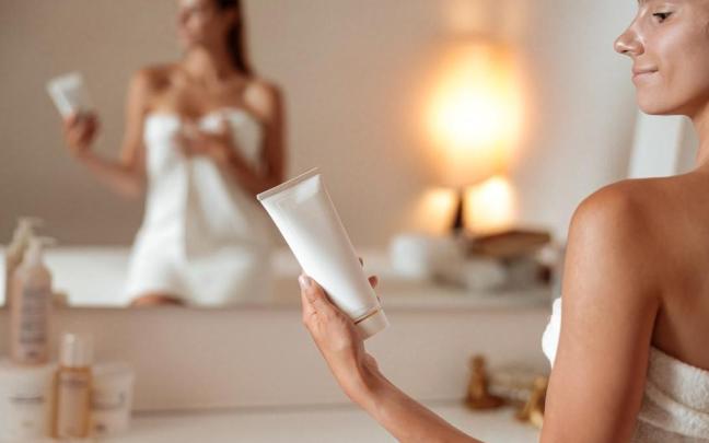 Chica sostiene un bote de crema en la mano nada más salir de la ducha.