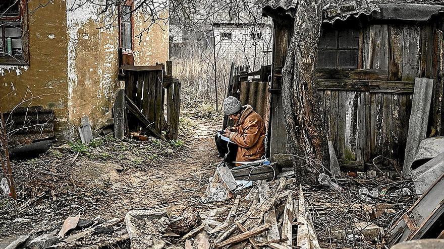 Una mujer usa su teléfono móvil para tomar notas sentada entre lo que queda de su casa destruida por los ataques en Bajmut.