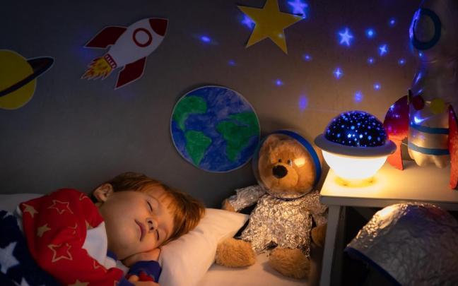 Un niño duerme con una luz nocturna sobre la mesa.